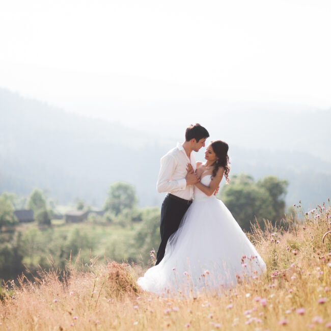 Hochzeitspaar tanzt auf einer Bergwiese vor Alpenkulisse