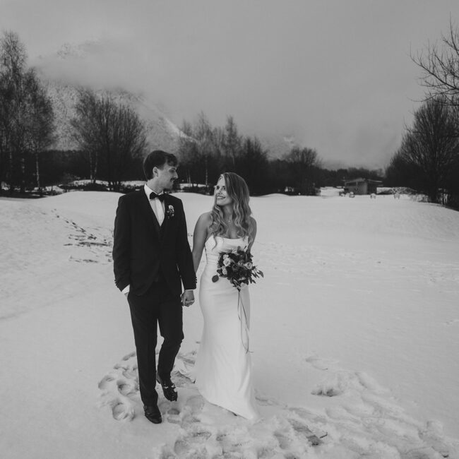 wedding couple walking through snowy alpine meadow