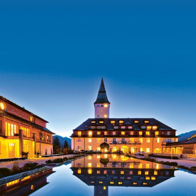 Schloss Elmau Hideaway illuminated at dusk with reflecting pool in the Bavarian Alps