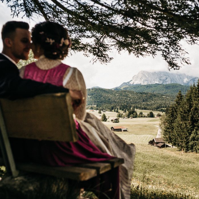 couple sitting in alpine meadow overlooking mountain landscape during wedding